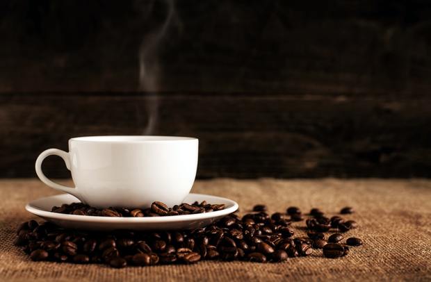 A steaming cup of coffee on top of coffee beans