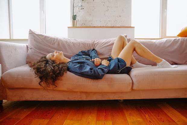 A woman lies on the sofa holding her abdomen in pain