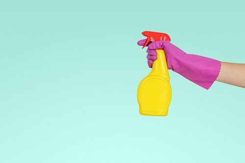 A gloved hand spraying a bottle of cleaner