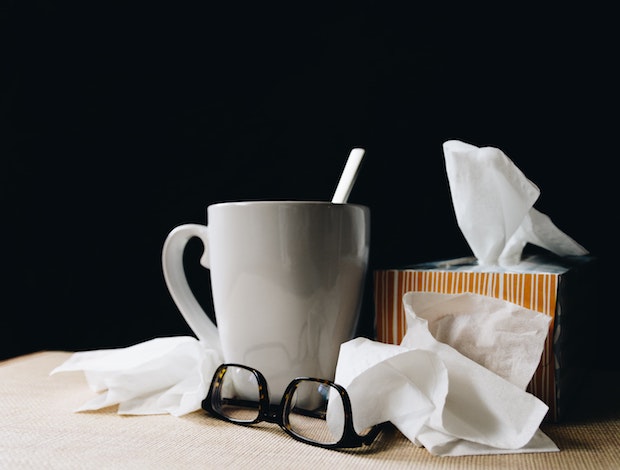 crumpled-up tissues next to a cup of tea and eye glasses