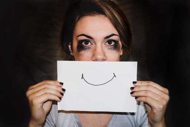 a woman with smudged eye makeup holding a paper with a smiley face in front of her face